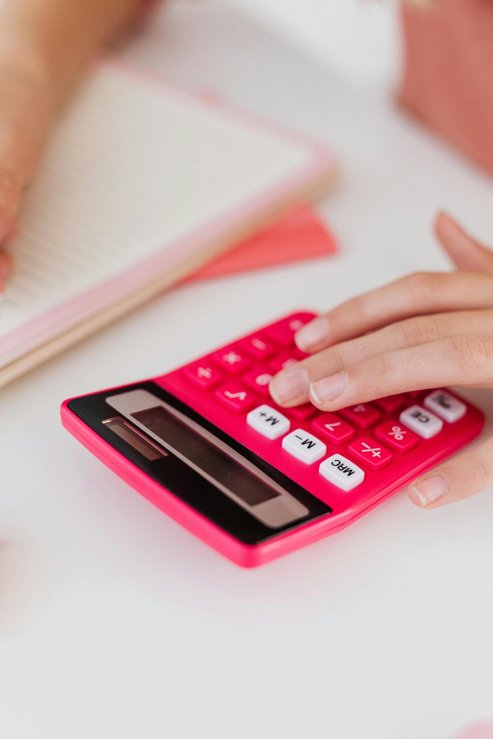 Close-up of hands using a pink calculator on a desk, emphasizing learning and education concepts.