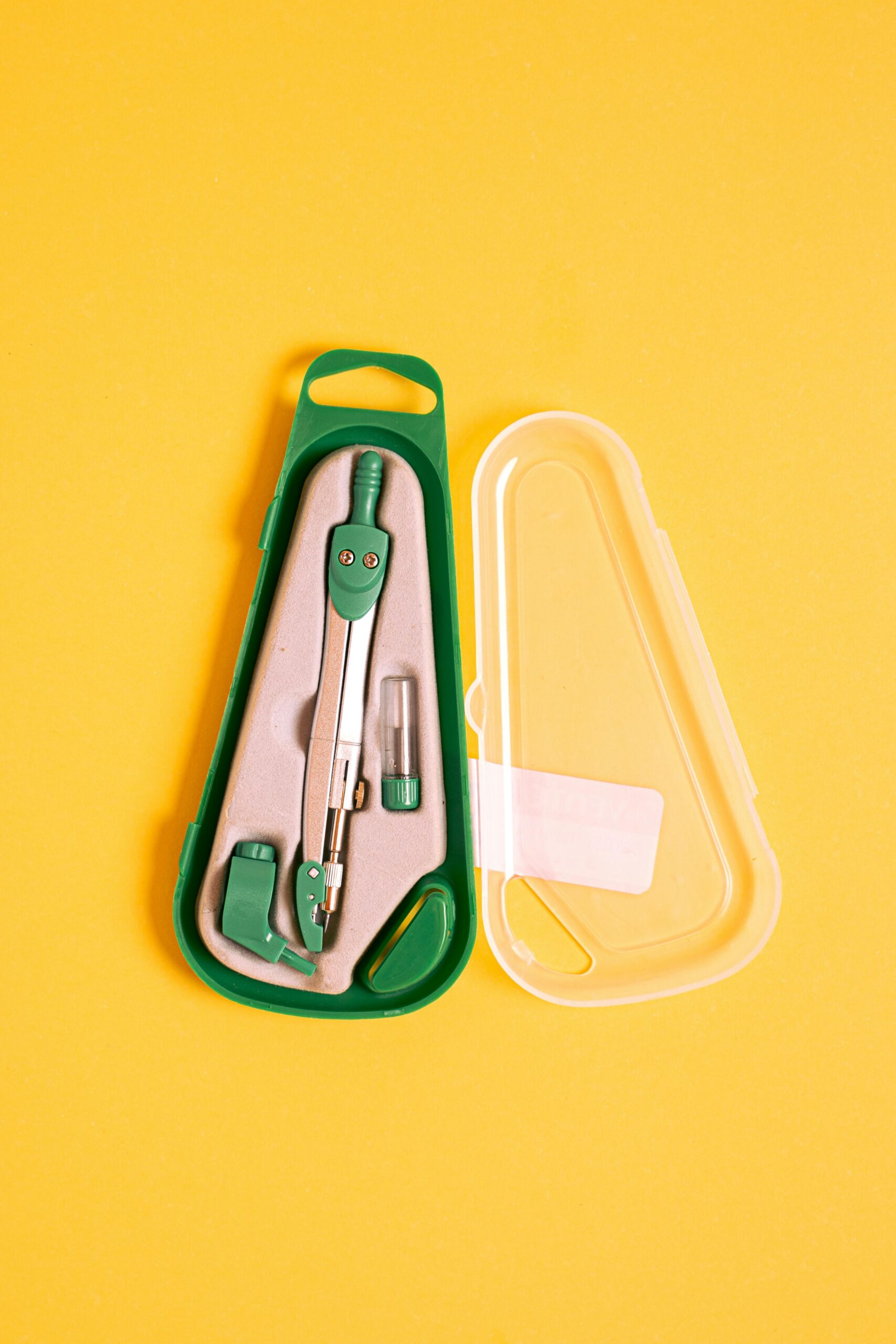 Green geometry compass in a plastic case on a vibrant yellow background.